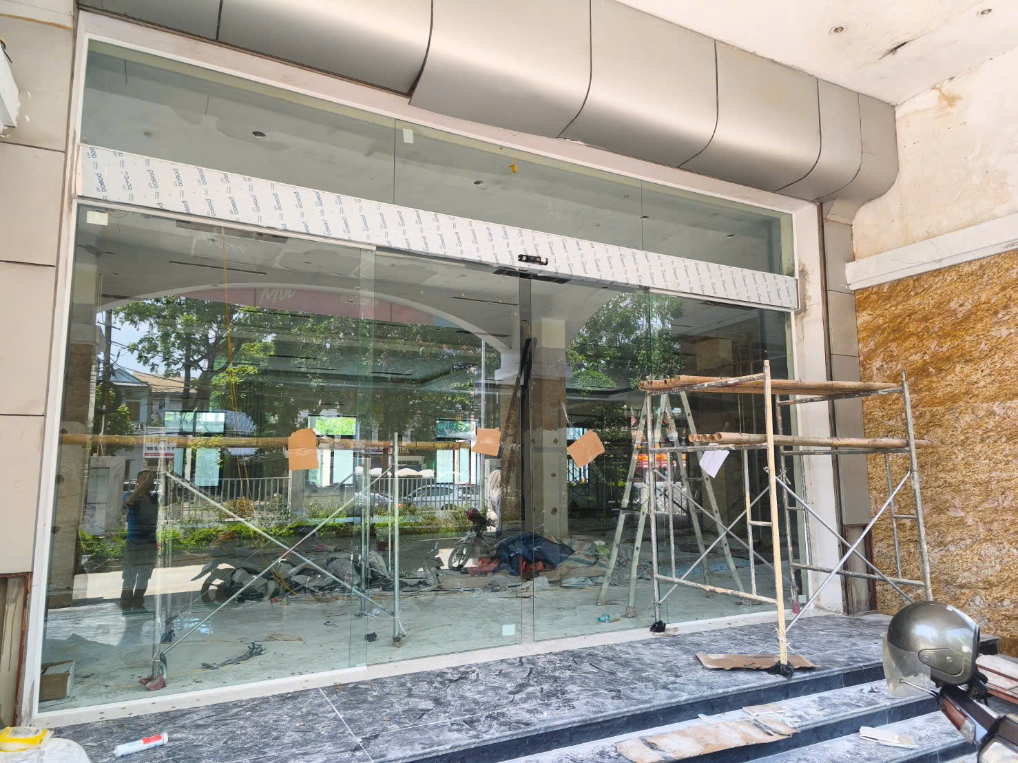 Cửa kính cường lực mặt tiền cửa hàng đang thi công với giàn giáo và thợ lắp đặt bên trong